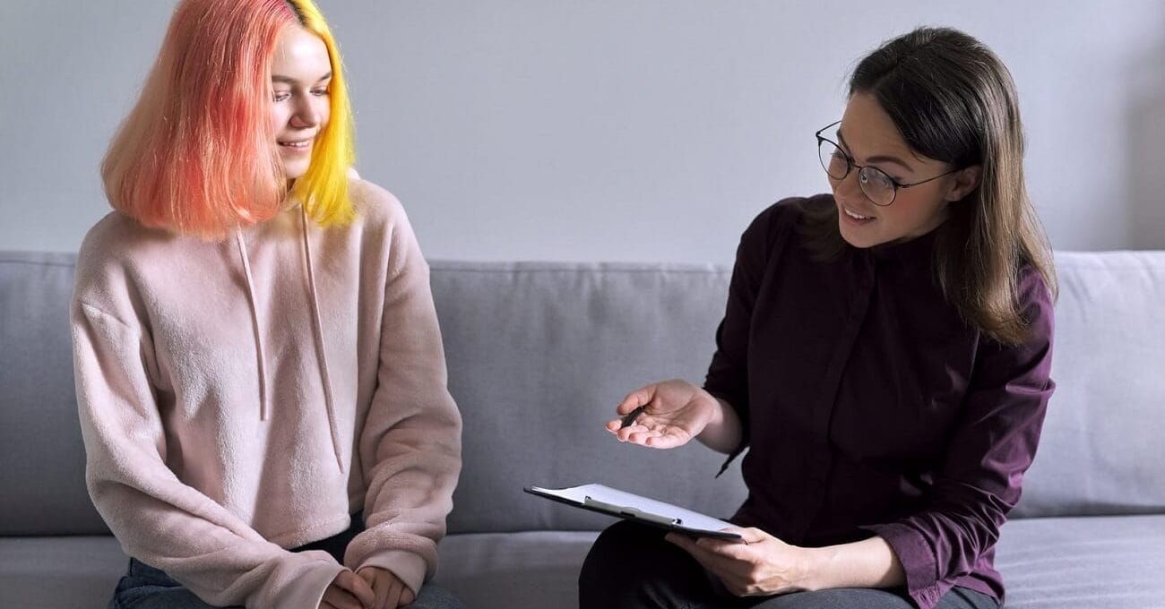 adolescente de cabelo rosa dando entrevista sentada no sofá de casa