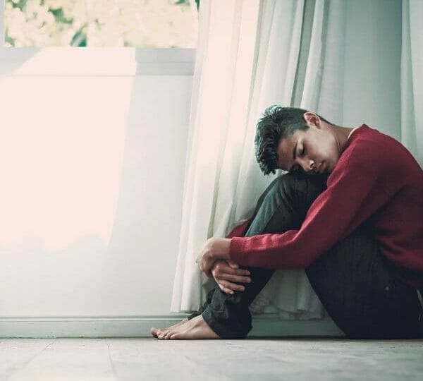 Adolescente triste sentado no chão com a cabeça encostada nos joelhos e abraçando as pernas