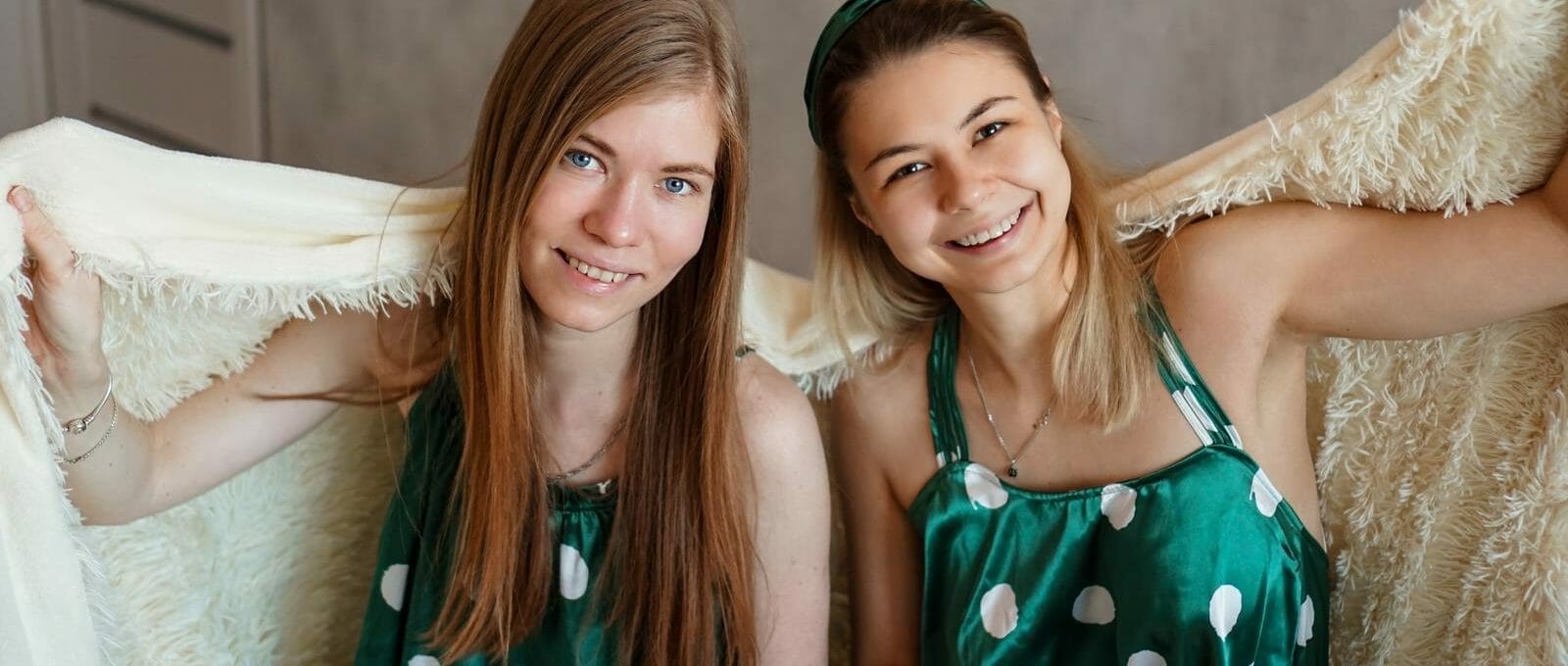 Duas adolescentes sorrindo embaixo de um cobertor enquanto estão dormindo fora de casa