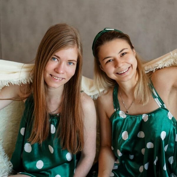 Duas adolescentes sorrindo embaixo de um cobertor enquanto estão dormindo fora de casa