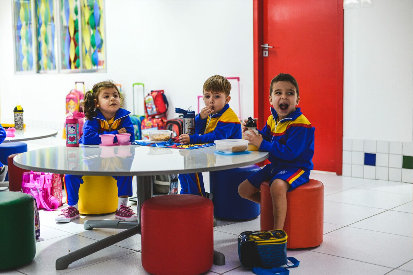 três crianças de uniforme comendo no refeitório do Alfa CEM Arena