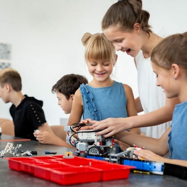 crianças e adolescentes em uma mesa trabalhando em um robô durante uma aula de programação em escola inovadora