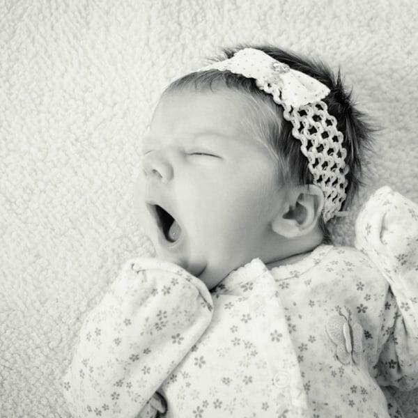 foto preta e branca de bebê dormindo no berço e bocejando