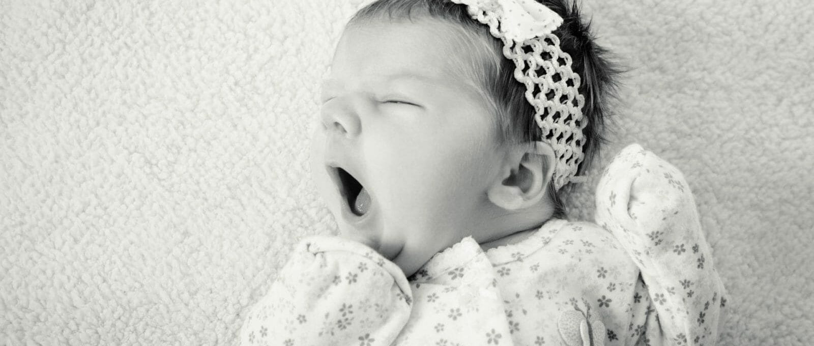 foto preta e branca de bebê dormindo no berço e bocejando