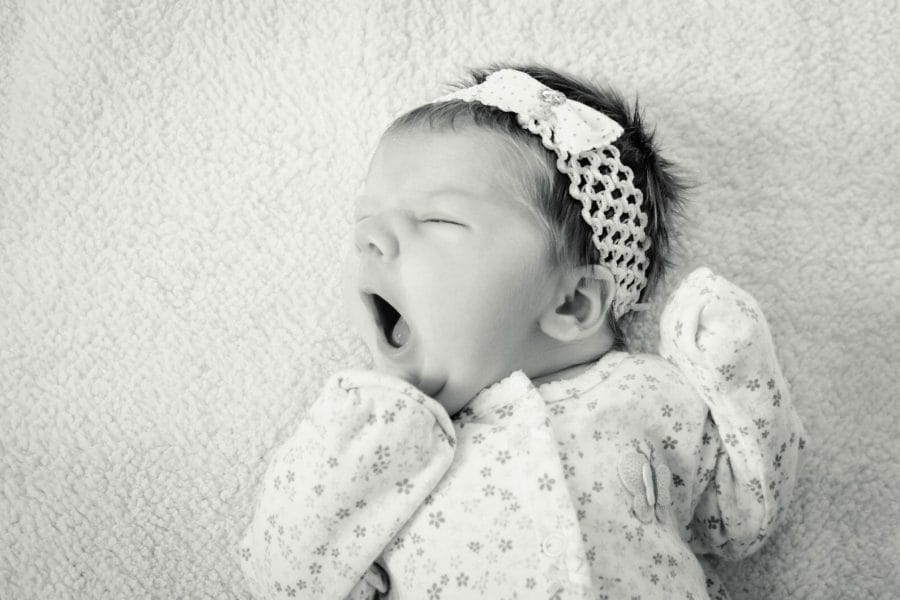 foto preta e branca de bebê dormindo no berço e bocejando