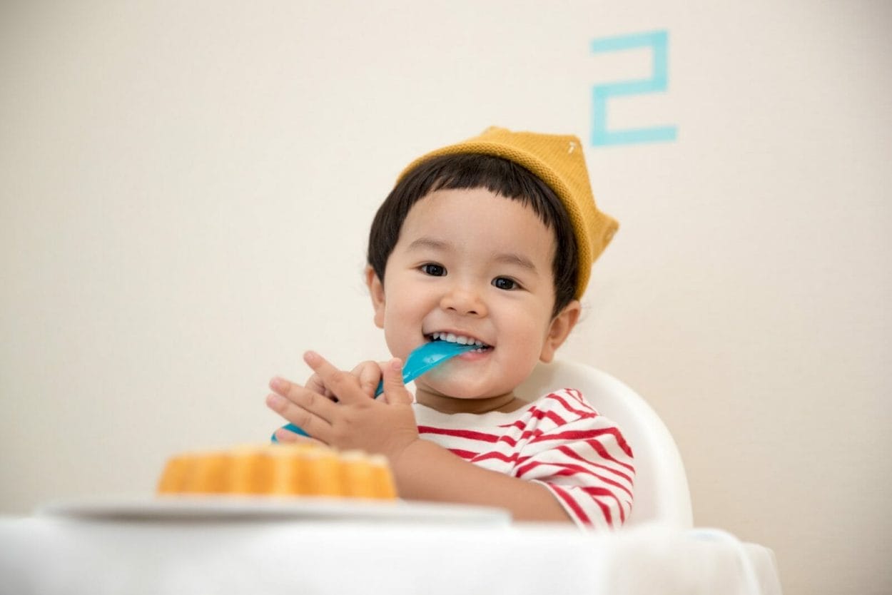 Bebê com colher na boca, se preparando para comer bolo de aniversário