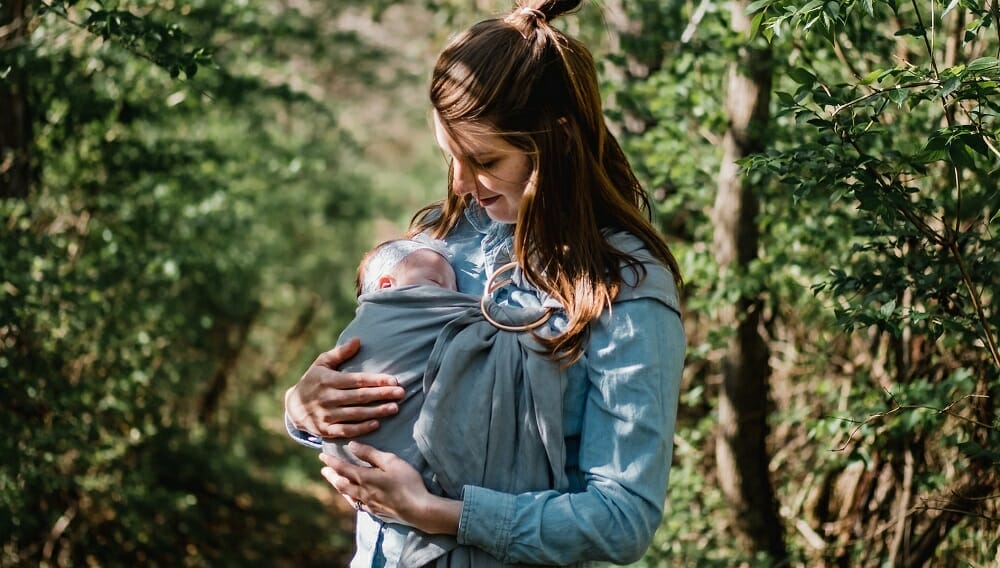 mãe carregando um bebê com um sling em um bosque