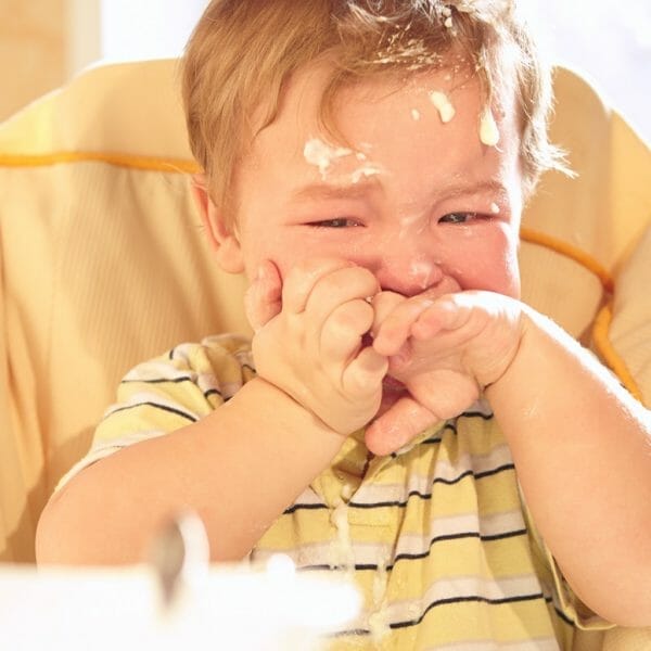 Bebê chorando sentado na cadeirinha, sujo de comida