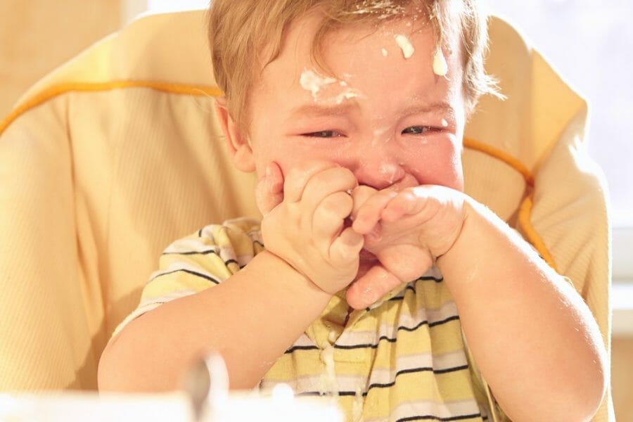 Bebê chorando sentado na cadeirinha, sujo de comida