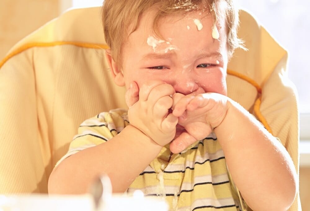 Bebê chorando sentado na cadeirinha, sujo de comida