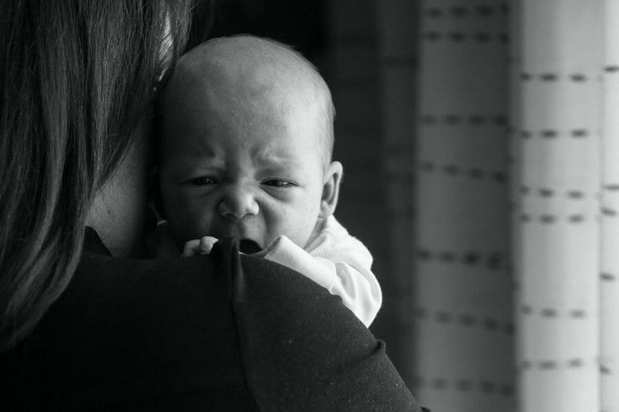 Bebê resfriado chorando no colo da mãe; fotografia em preto e branco