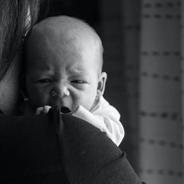Bebê resfriado chorando no colo da mãe; fotografia em preto e branco