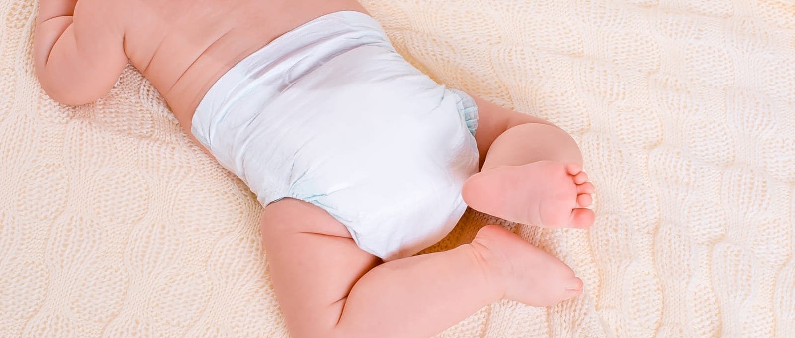 bebê deitado na cama de bruços usando fraldas brancas