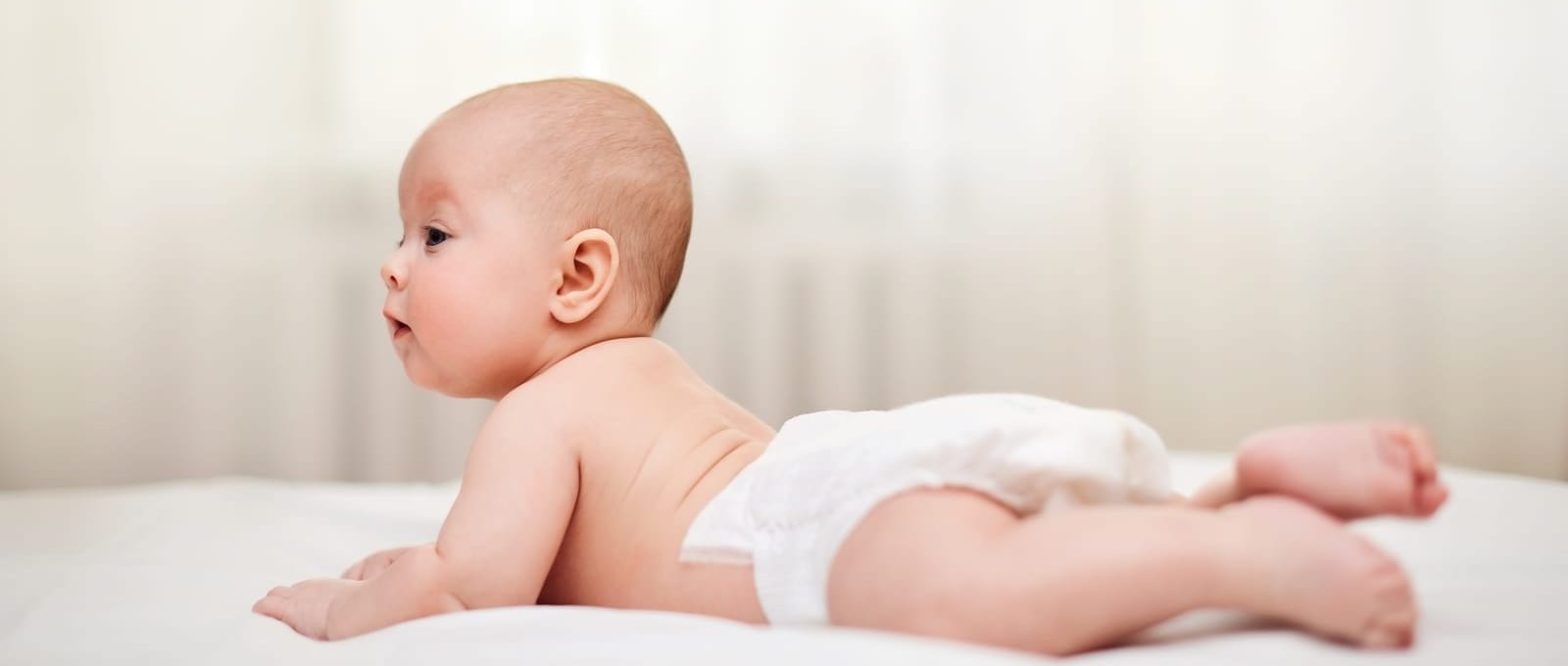bebê deitado de bruços na cama usando fraldas