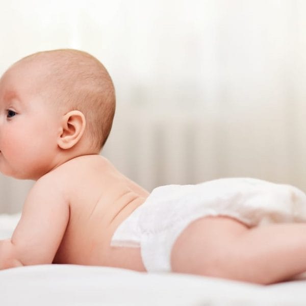 bebê deitado de bruços na cama usando fraldas