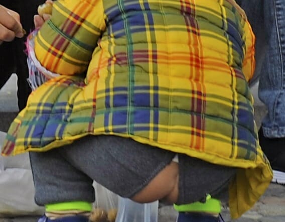 criança agachada no chão usando uma calça aberta para método chinês de desfraldar