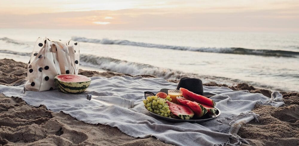 piquenique na praia, com cesta de frutas e sacola para levar os alimentos