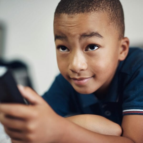 Criança deitada na cama com controle remoto nas mãos, representando o conceito de controlar o próprio tempo de tela