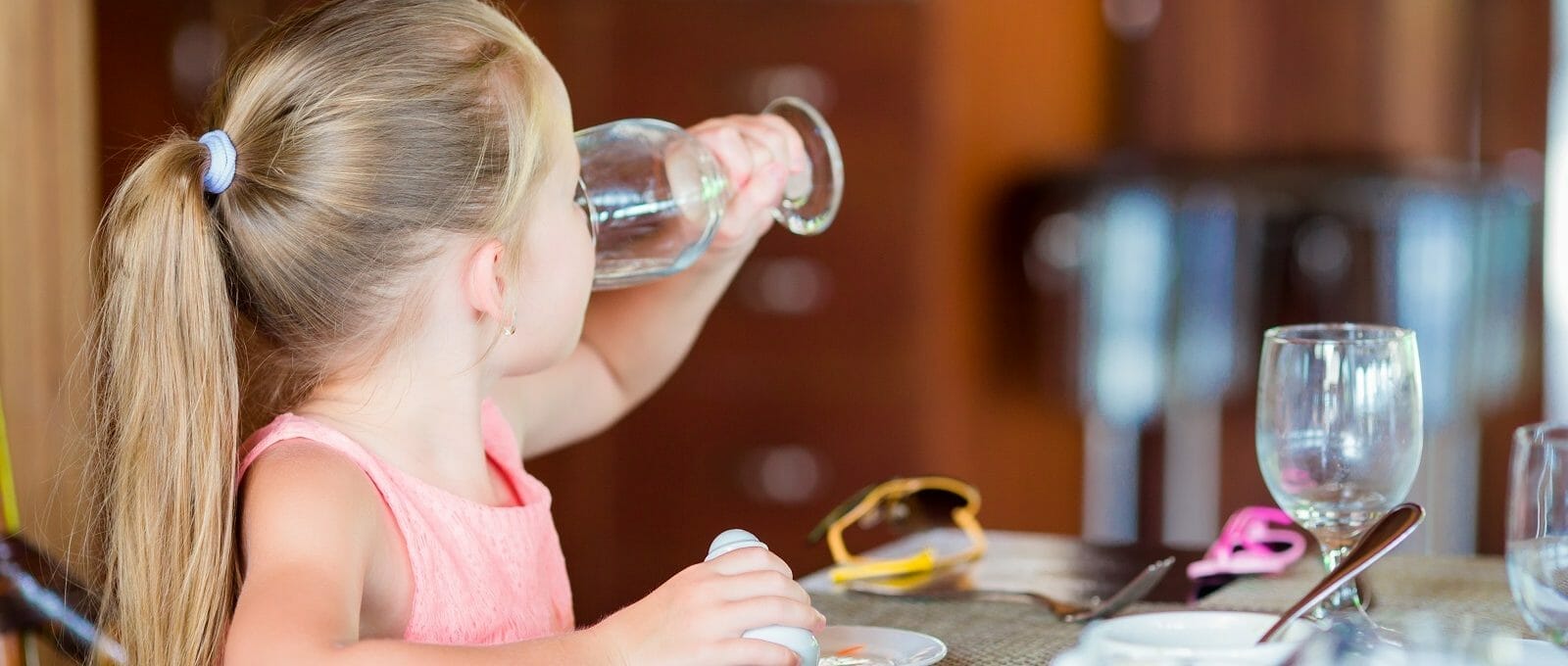 menina bebendo uma taça de água durante o café da manhã em um restaurante