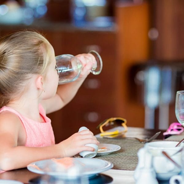 menina bebendo uma taça de água durante o café da manhã em um restaurante