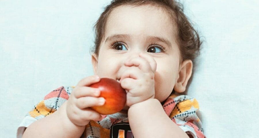 Criança brincando com fruta na boca