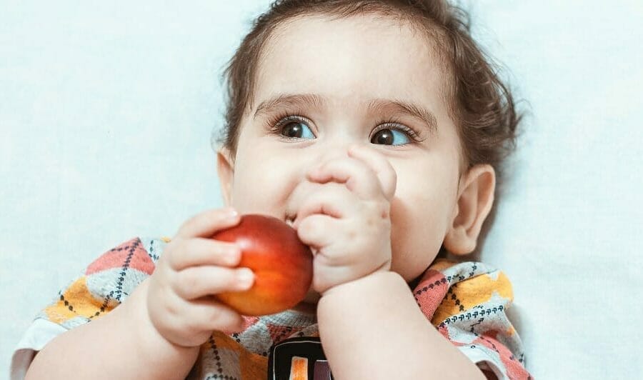Criança brincando com fruta na boca