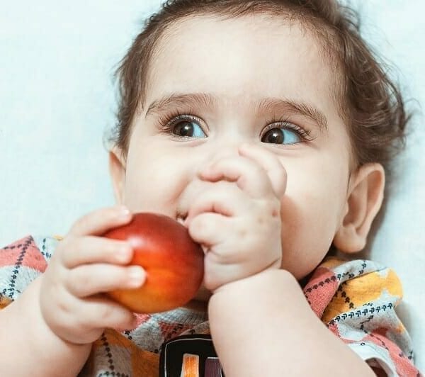 Criança brincando com fruta na boca