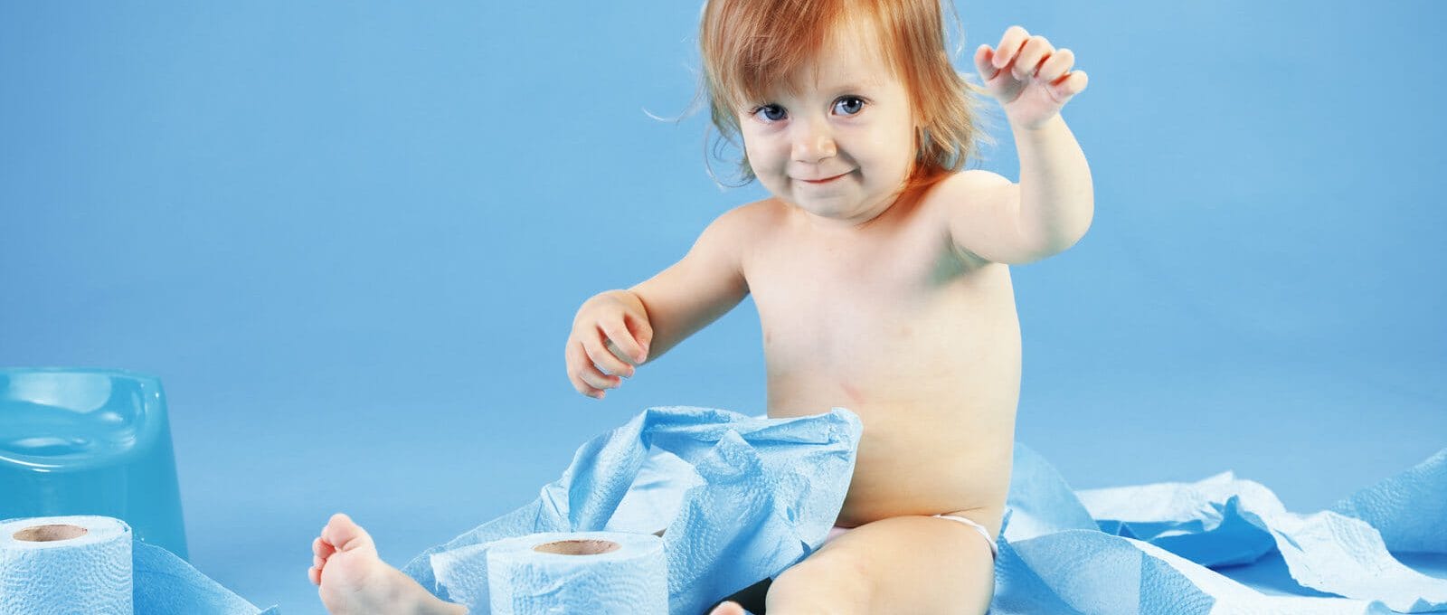 criança sentada em um cenário azul, brincando com rolos de papeis higiênicos azuis durante o desfralde