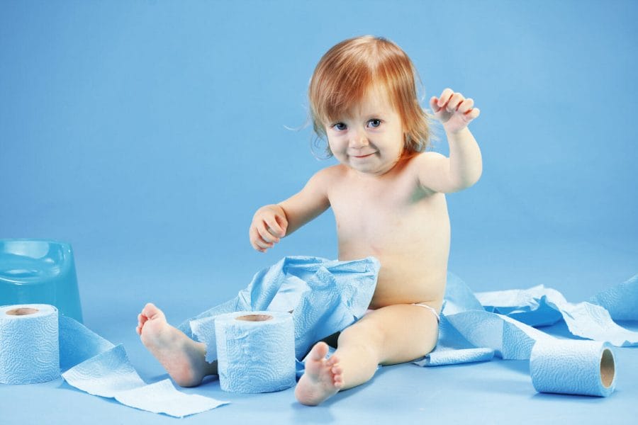 criança sentada em um cenário azul, brincando com rolos de papeis higiênicos azuis durante o desfralde