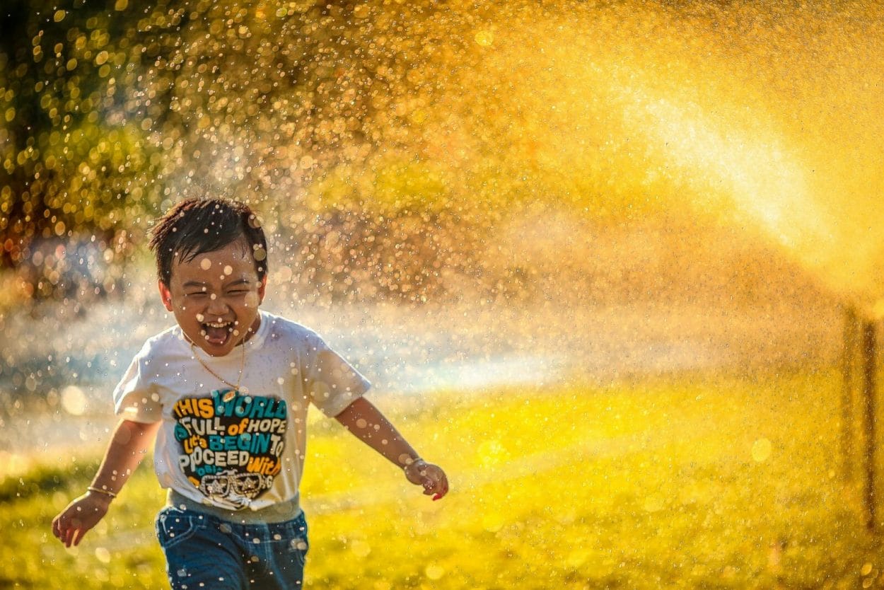 criança correndo ao lado de irrigadores no final da tarde