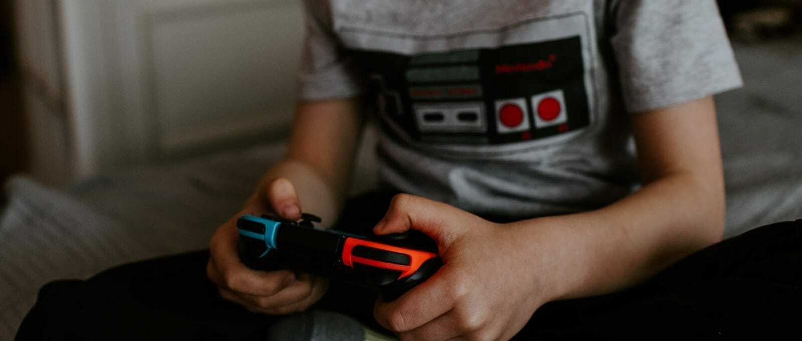 criança usando uma camisa com estampa de controle de videogame e segurando um controle nas mãos