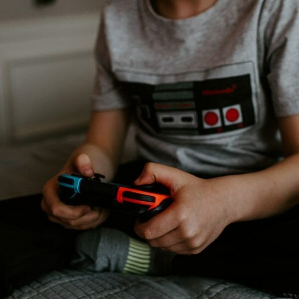 criança usando uma camisa com estampa de controle de videogame e segurando um controle nas mãos