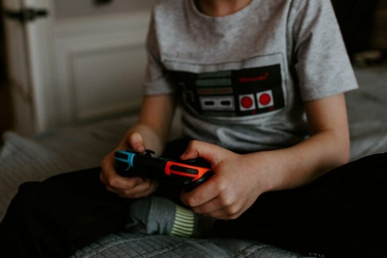 criança usando uma camisa com estampa de controle de videogame e segurando um controle nas mãos