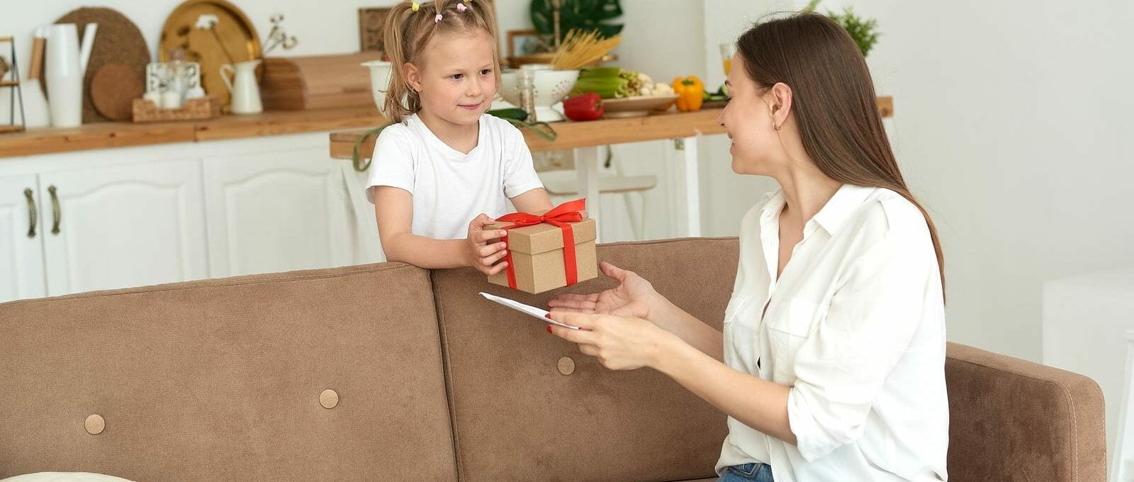 mãe sentada no sofá recebendo caixinha de presente da filha