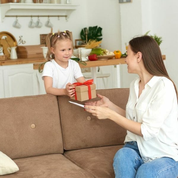 mãe sentada no sofá recebendo caixinha de presente da filha