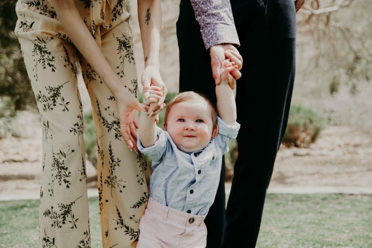 pais segurando um bebê vestindo roupas sociais pelos bracinhos em festa