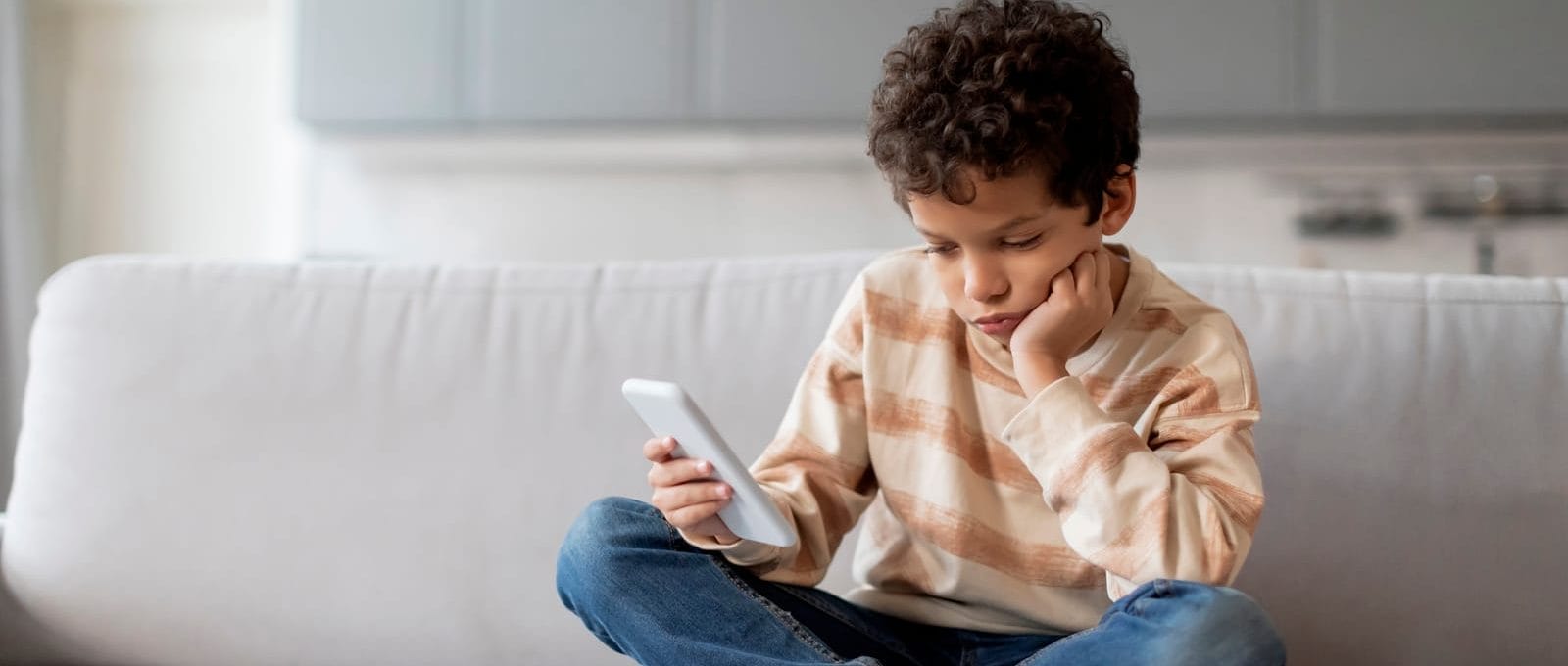 criança sentada no sofá olhando emburrada para o celular