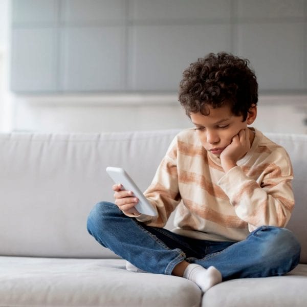 criança sentada no sofá olhando emburrada para o celular