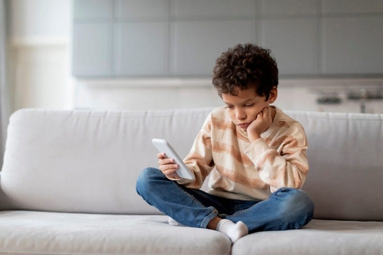 criança sentada no sofá olhando emburrada para o celular