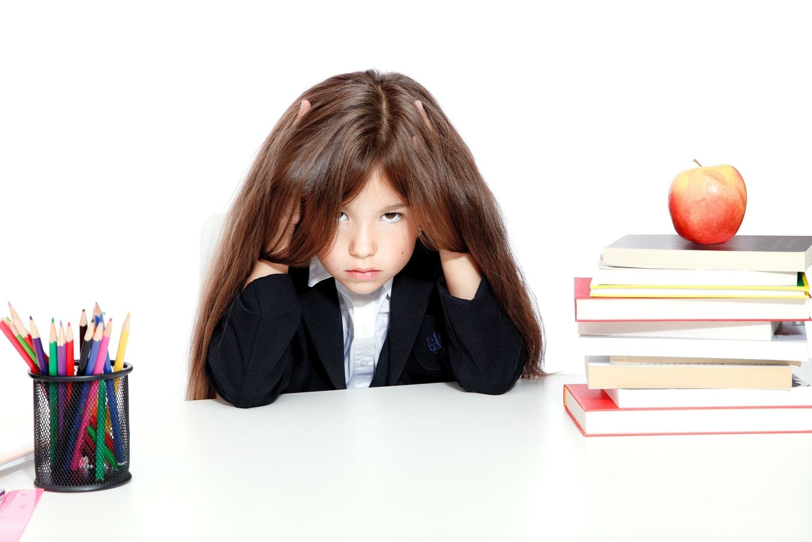 criança frustrada com os estudos, com expressão aborrecida, ao lado de uma pilha de livros com uma maçã em cima, e um porta-lápis do outro lado