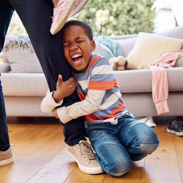 Criança fazendo birra ao desligar a televisão, ajoelhada no chão, agarrada na perna da mãe e gritando
