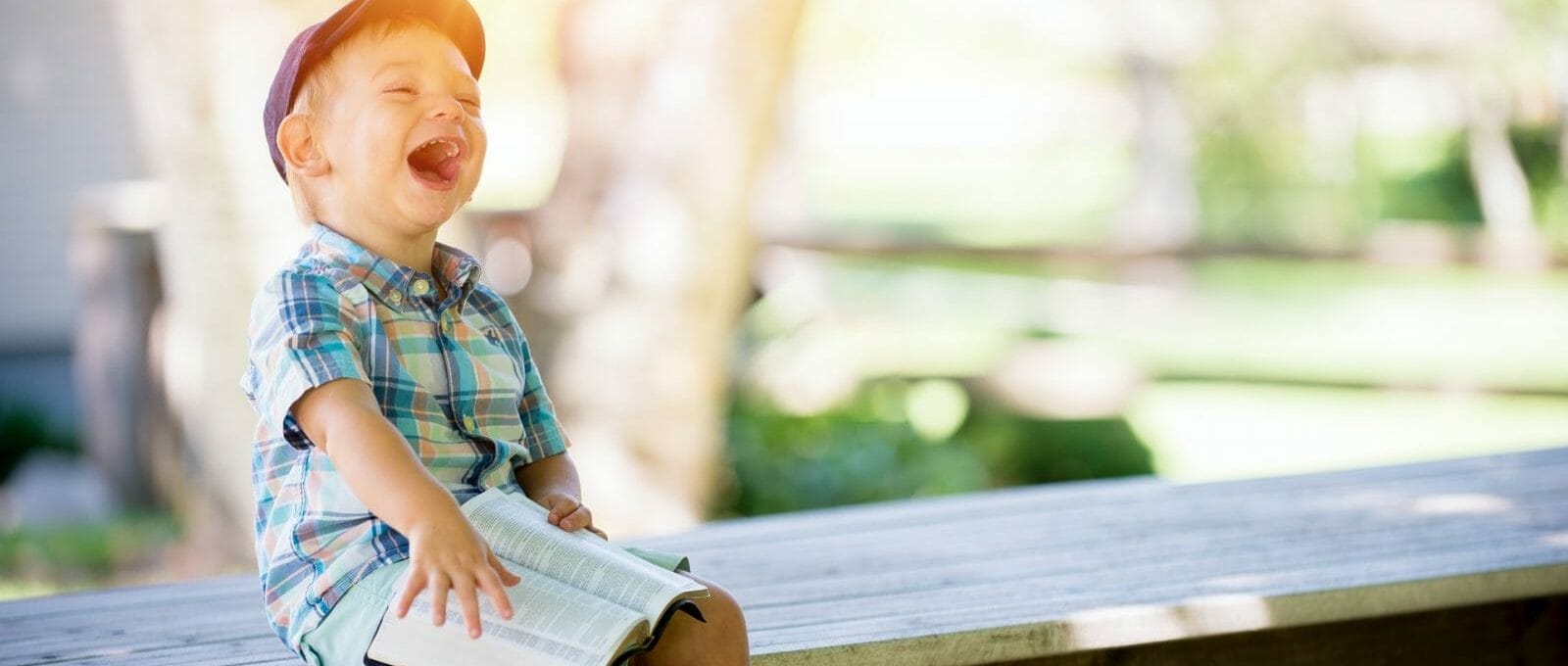 criança sorrindo em um banco ao ar livre com um livro no colo