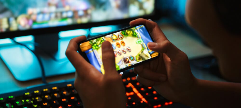 Criança se divertindo jogando no celular, com computador gamer ligado no fundo