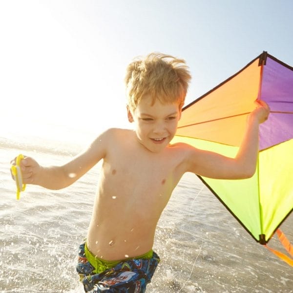 criando correndo na praia com uma pipa na mão, representando o conceito de como soltar pipa