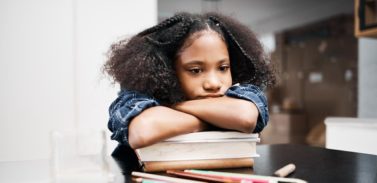 Criança apoiada em cima de uma pilha de livros com expressão triste e desanimada no rosto