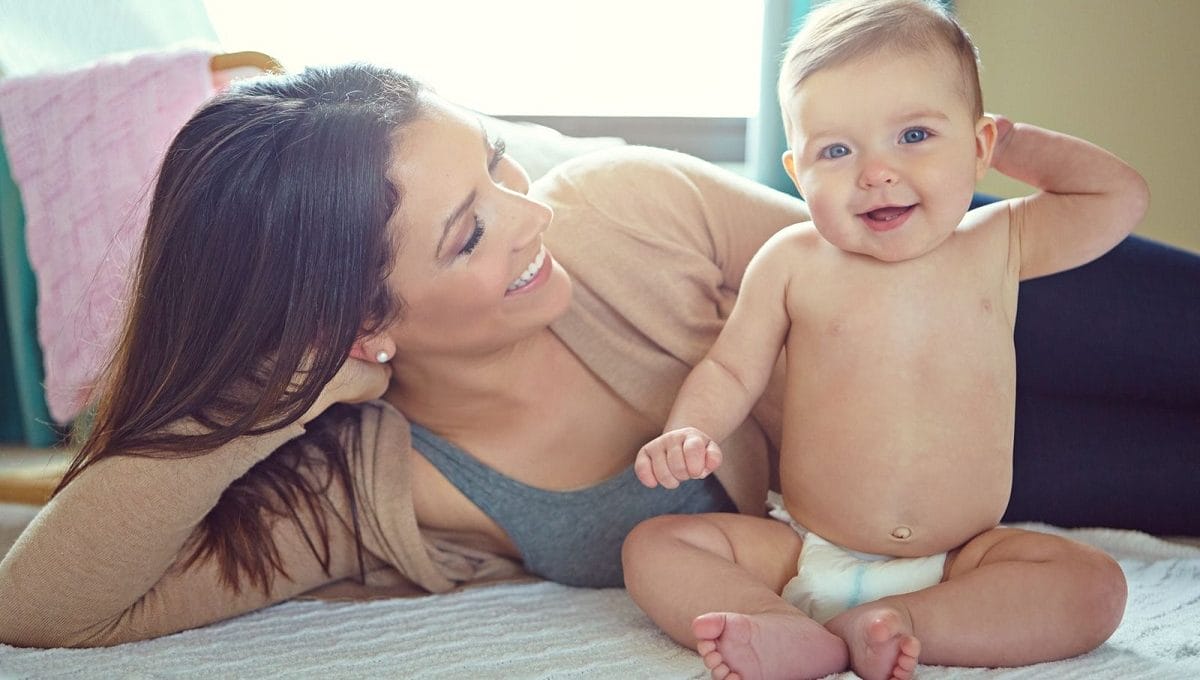 mãe deitada na cama ao lado de um bebê usando fraldas descartáveis