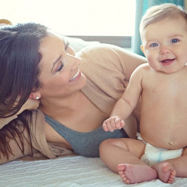 mãe deitada na cama ao lado de um bebê usando fraldas descartáveis
