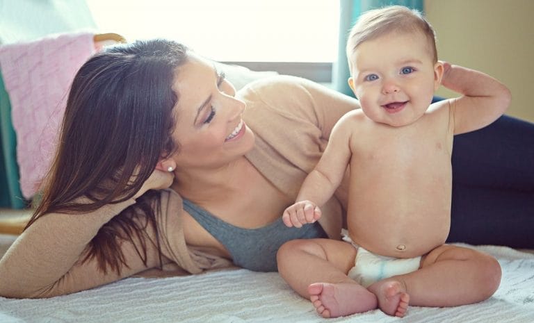 mãe deitada na cama ao lado de um bebê usando fraldas descartáveis
