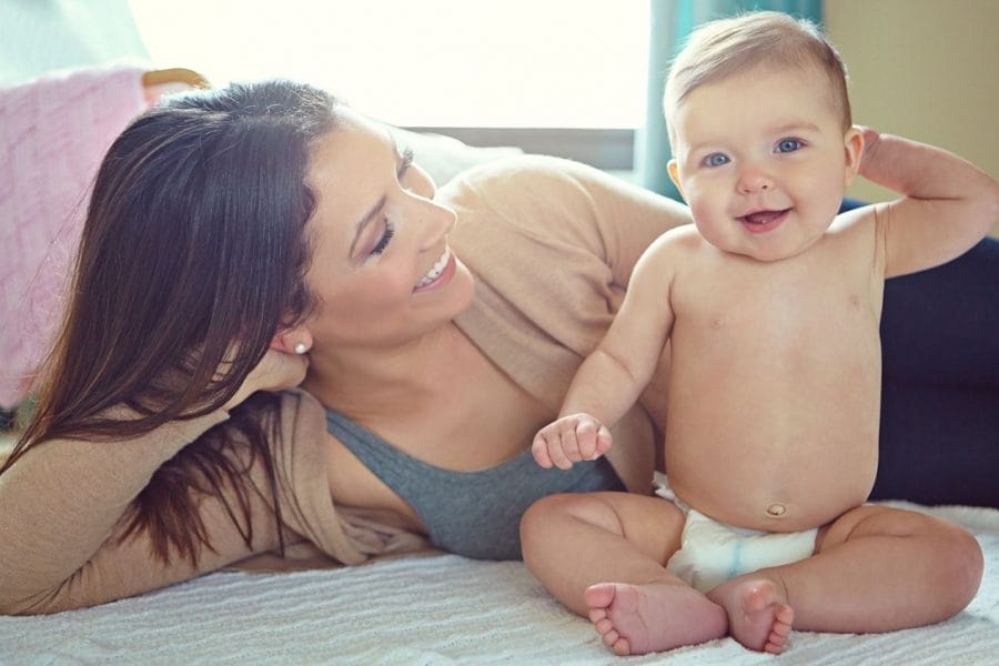 mãe deitada na cama ao lado de um bebê usando fraldas descartáveis