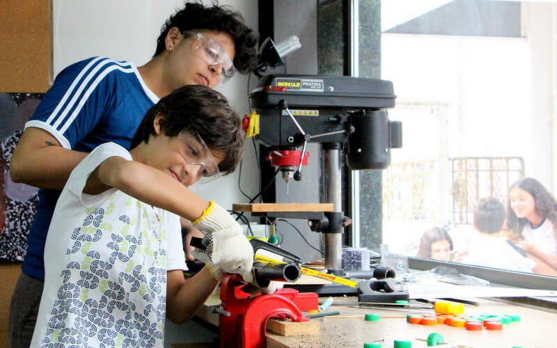 aluno do ensino fundamental fazendo trabalhos manuais na mesa com orientação de educadora